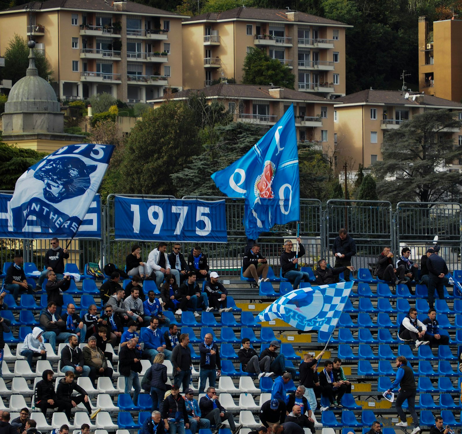 Como 1907 supporters sitting below blue flags in the Sinigaglia stands