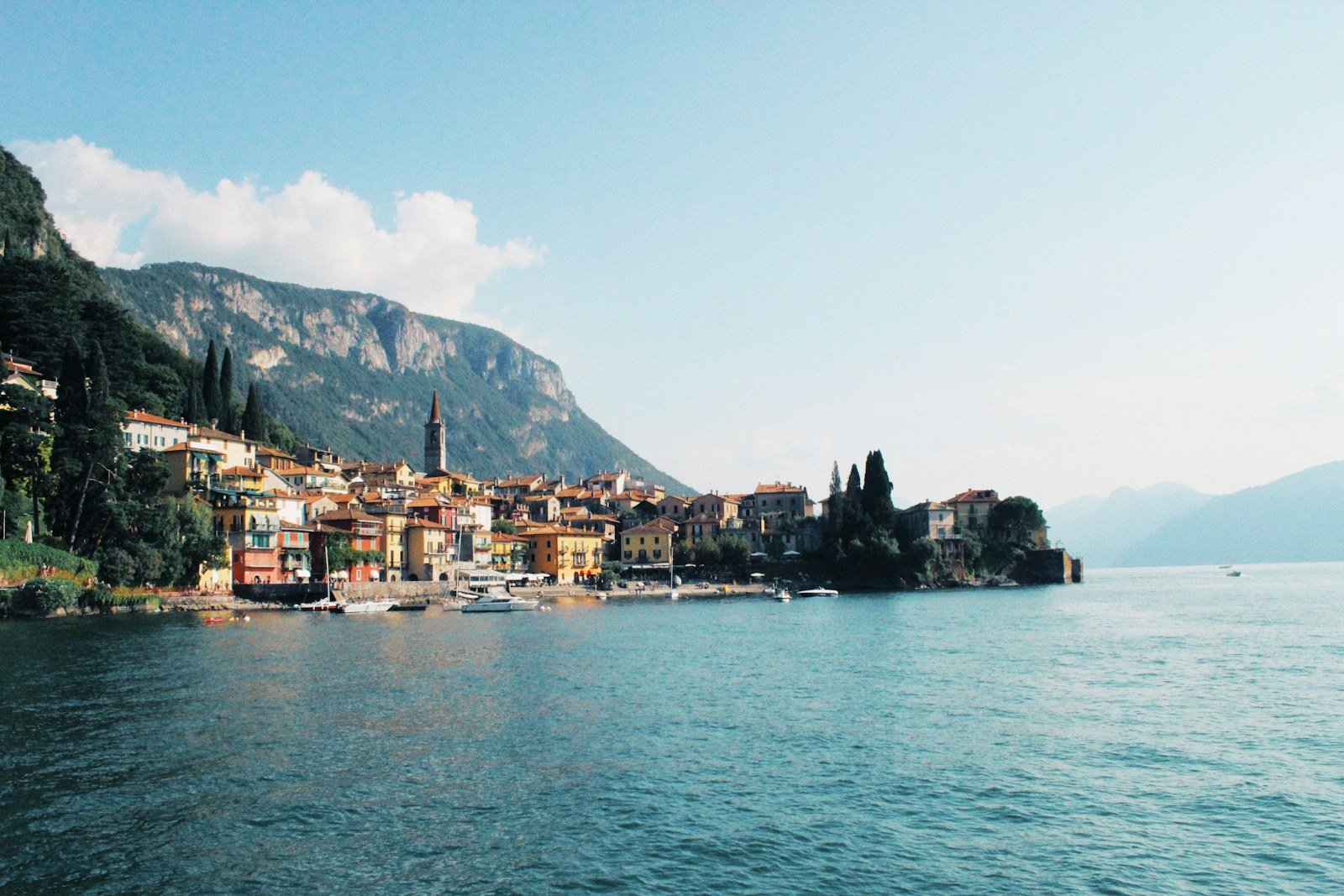 A village on Lake Como with boats on the water and mountains behind it
